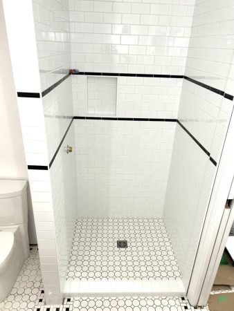 Subway tile shower with black accent band, niche box, octagon and dot floor